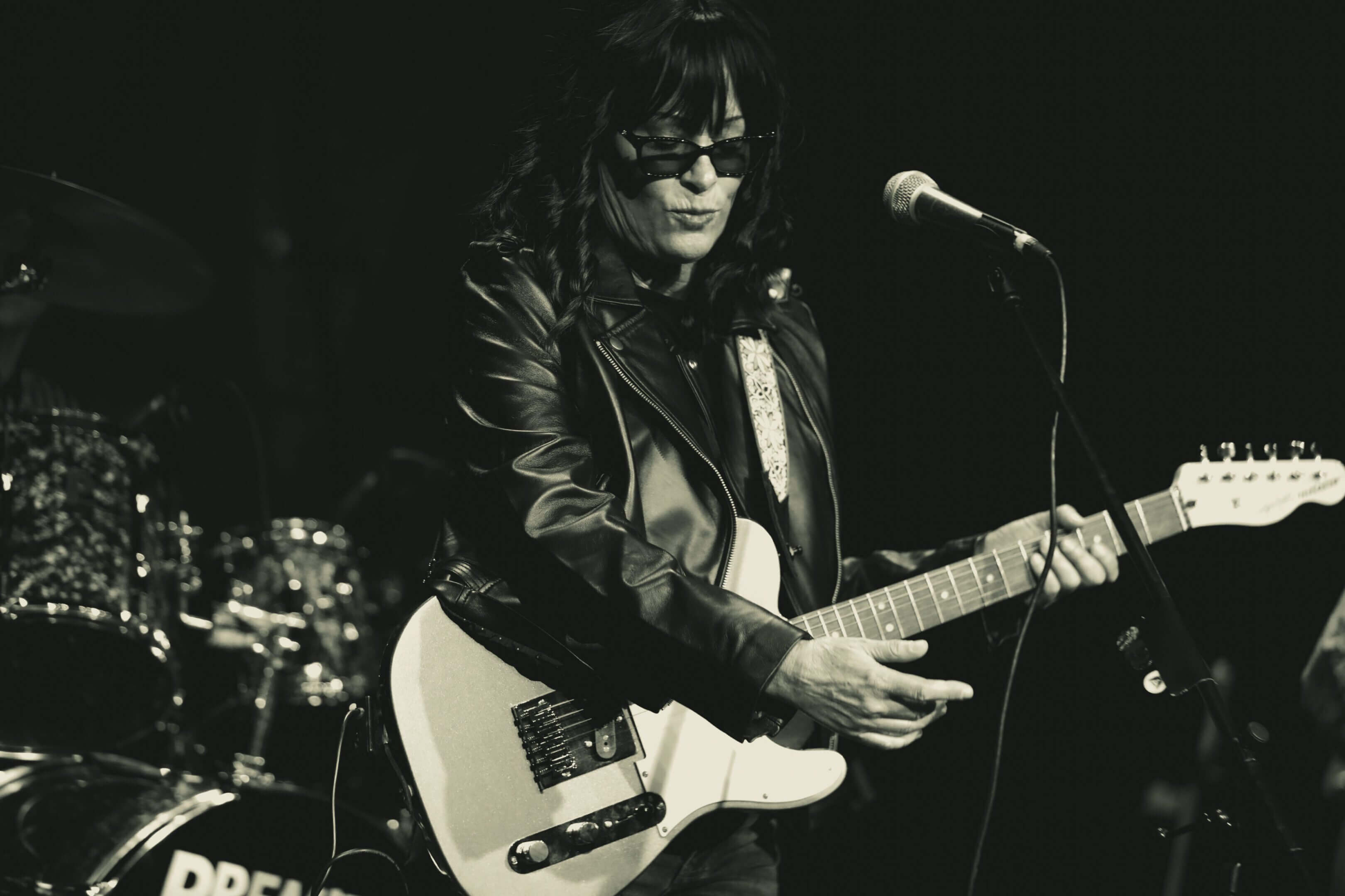 Musician playing electric guitar on stage in black leather jacket.