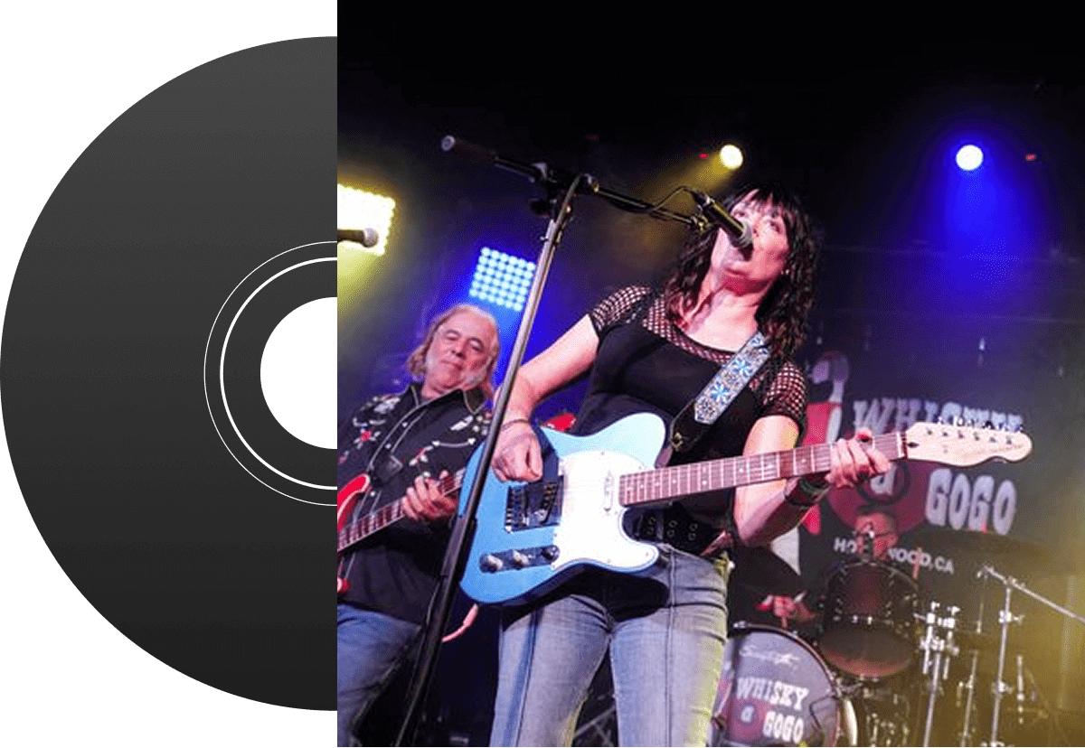 A female guitarist passionately performing on stage with a male bassist in the background.