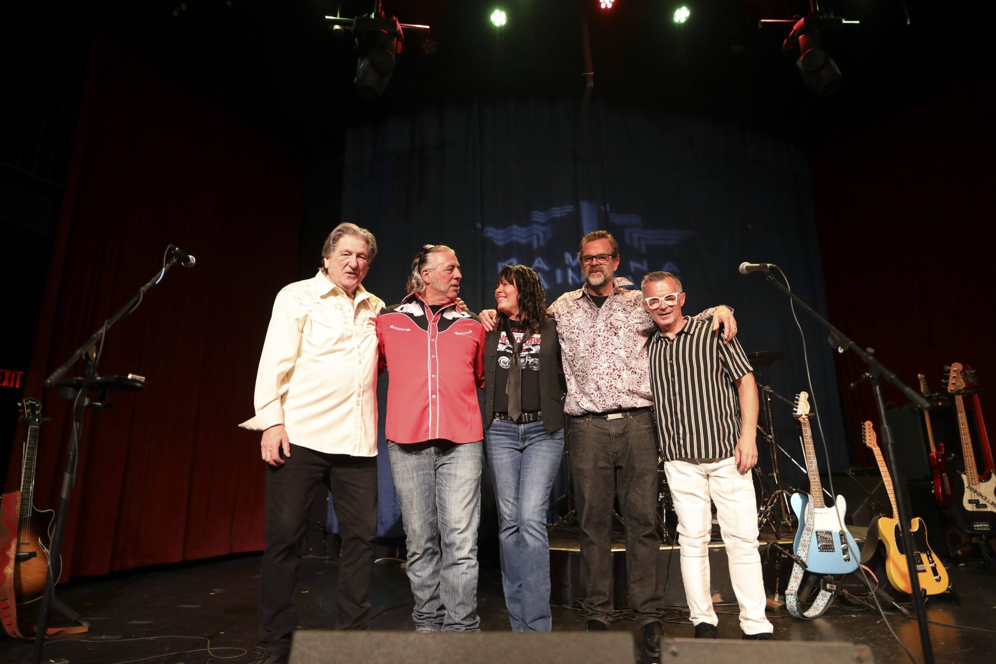 Five men posing together on stage under spotlights.